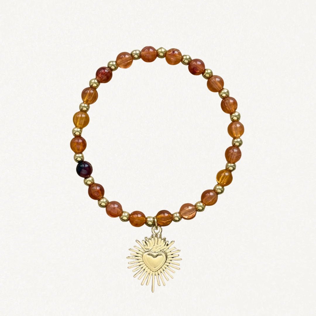 Bracelet fin perles Oranges avec pendentif cœur sacré doré sur fond blanc.