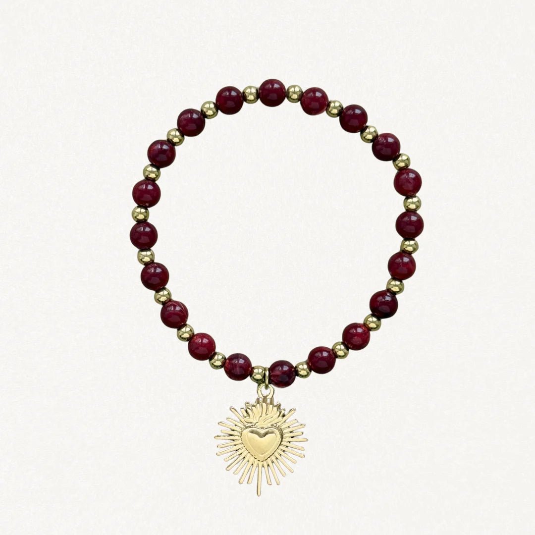 Bracelet fin perles Bordeaux avec pendentif cœur sacré doré sur fond blanc.