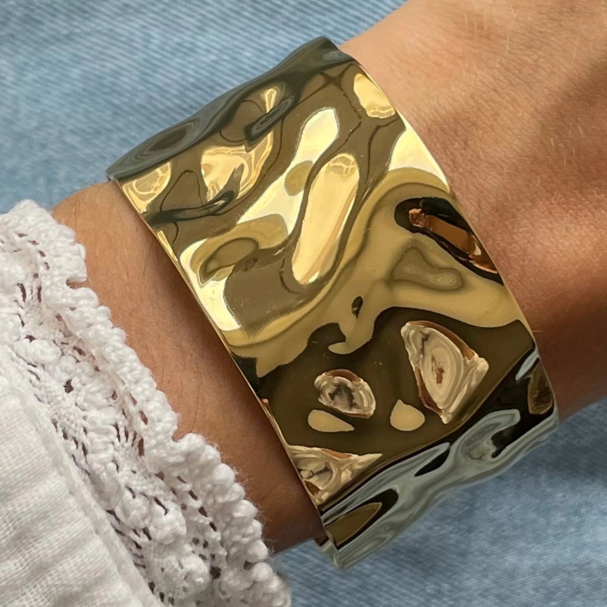 Gros plan bracelet manchette large Sofia en acier inoxydable doré à effet martelé et surface irrégulière porté au poignet.