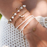 Lot de bracelets en acier inoxydable doré avec perles, coquillages et étoile de mer sur poignet féminin.