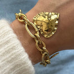 Gros plan bracelet grosse maille en acier inoxydable doré avec grand pendentif cœur texturé porté au poignet.