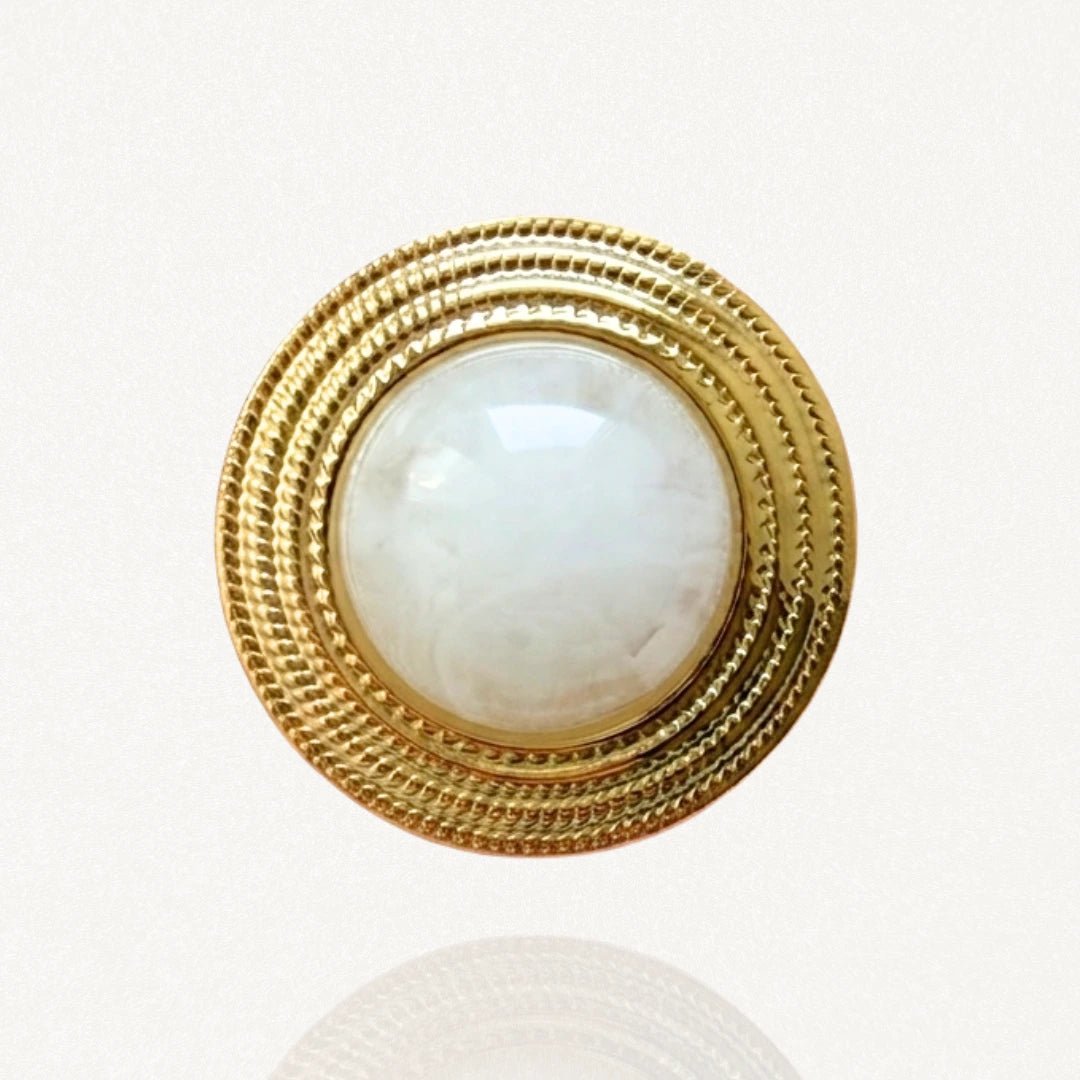 Broche classique Angela de face, monture dorée texturée et centre bombée en résine effet nacre sur fond blanc.