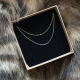 Coffret cadeau MAISON DE L'AMOUR présentant deux chaînes fines minimalistes (coloris or et argent) en acier inoxydable.