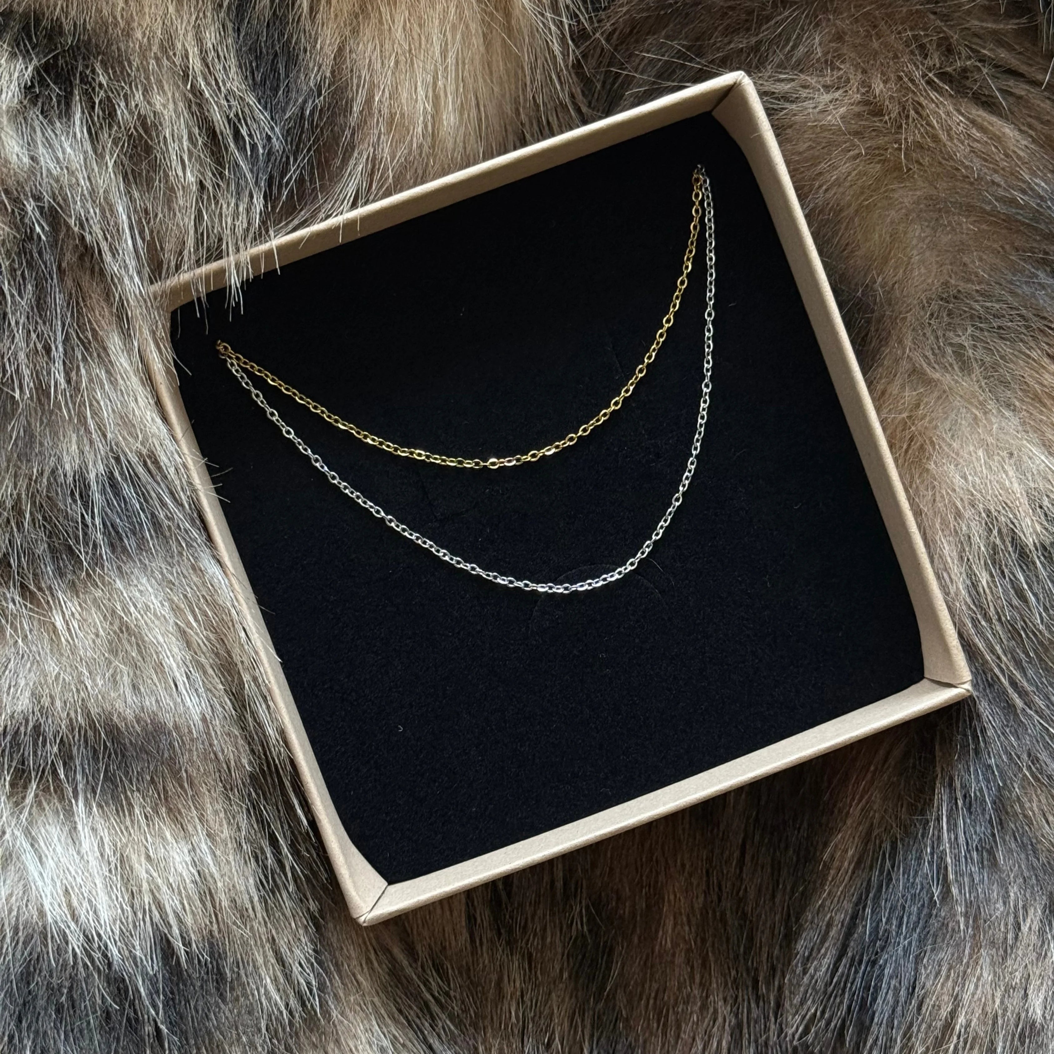 Coffret cadeau MAISON DE L'AMOUR présentant deux chaînes fines minimalistes (coloris or et argent) en acier inoxydable.