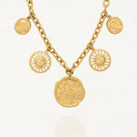 Collier à maillons épais couleur or, orné de cinq pendentifs. Un grand médaillon central avec une rose des vents, deux charms soleils souriants et deux pièces antiques.