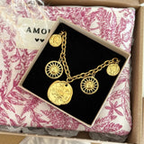 Bracelet chaîne dorée avec 2 charmes soleils, 2 médailles visages, 1 rose des vents, dans sa boîte noire sur tissu toile de Jouy.