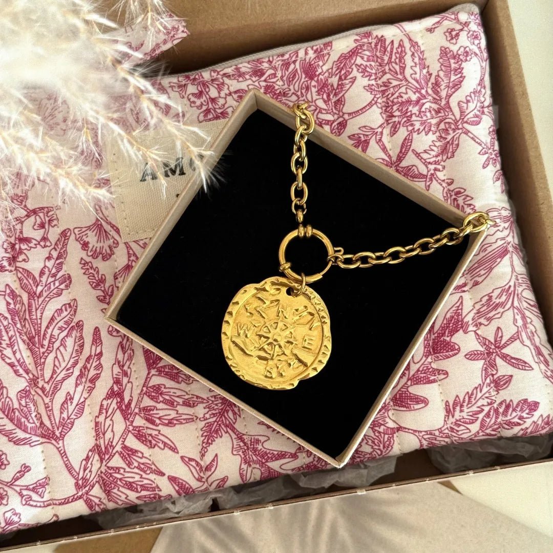 Collier doré à maillons épais, médaillon boussole gravé, dans boîte noire sur tissu matelassé rose motif Toile de Jouy.