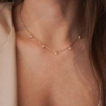 Collier ras-de-cou fin en acier inoxydable doré orné de petites perles blanches style pampilles, porté au cou.