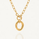 Collier BENEDICTE en acier inoxydable doré. Chaîne à maillons ovales, fermoir toggle et grand pendentif ovale de forme organique irrégulière. Posé sur fond blanc.