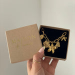 Collier à breloques nature et fleurs présenté dans sa boîte cadeau kraft Maison de l'Amour.