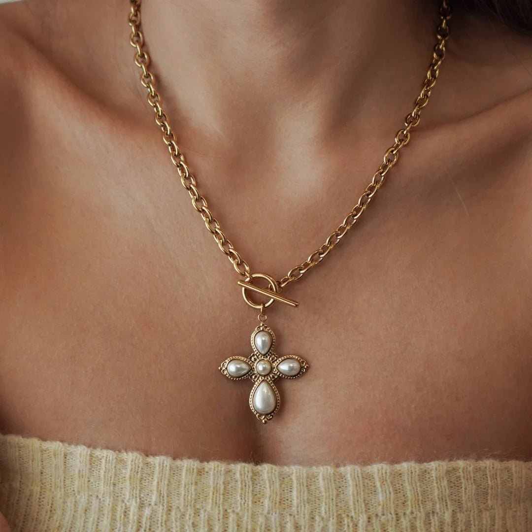 Collier grosse maille en acier inoxydable doré avec grand pendentif croix orné de perles et fermoir T porté sur le devant.
