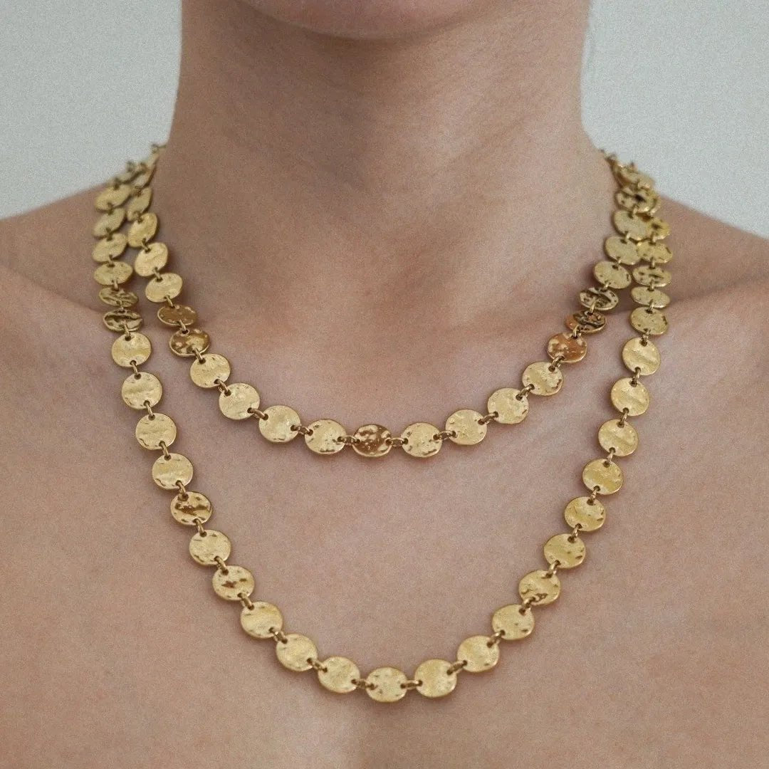Deux colliers dorés superposés, composés de pastilles rondes martelées, sur un décolleté.