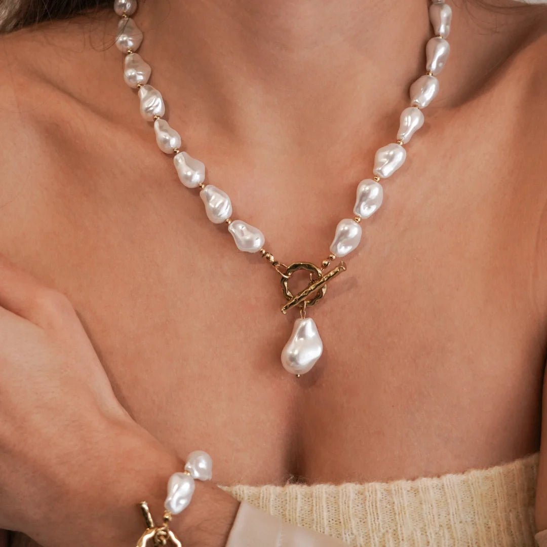 Collier de perles blanches style baroque irrégulier avec fermoir T (toggle) doré porté sur le devant en pendentif.