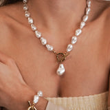 Collier de perles blanches style baroque irrégulier avec fermoir T (toggle) doré porté sur le devant en pendentif.