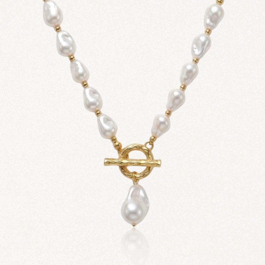 Collier en acier inoxydable doré avec perles baroques blanches, fermoir toggle et perle pendante.