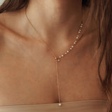 Collier forme Y plongeant avec chaîne fine dorée et petites perles blanches, style minimaliste et élégant.