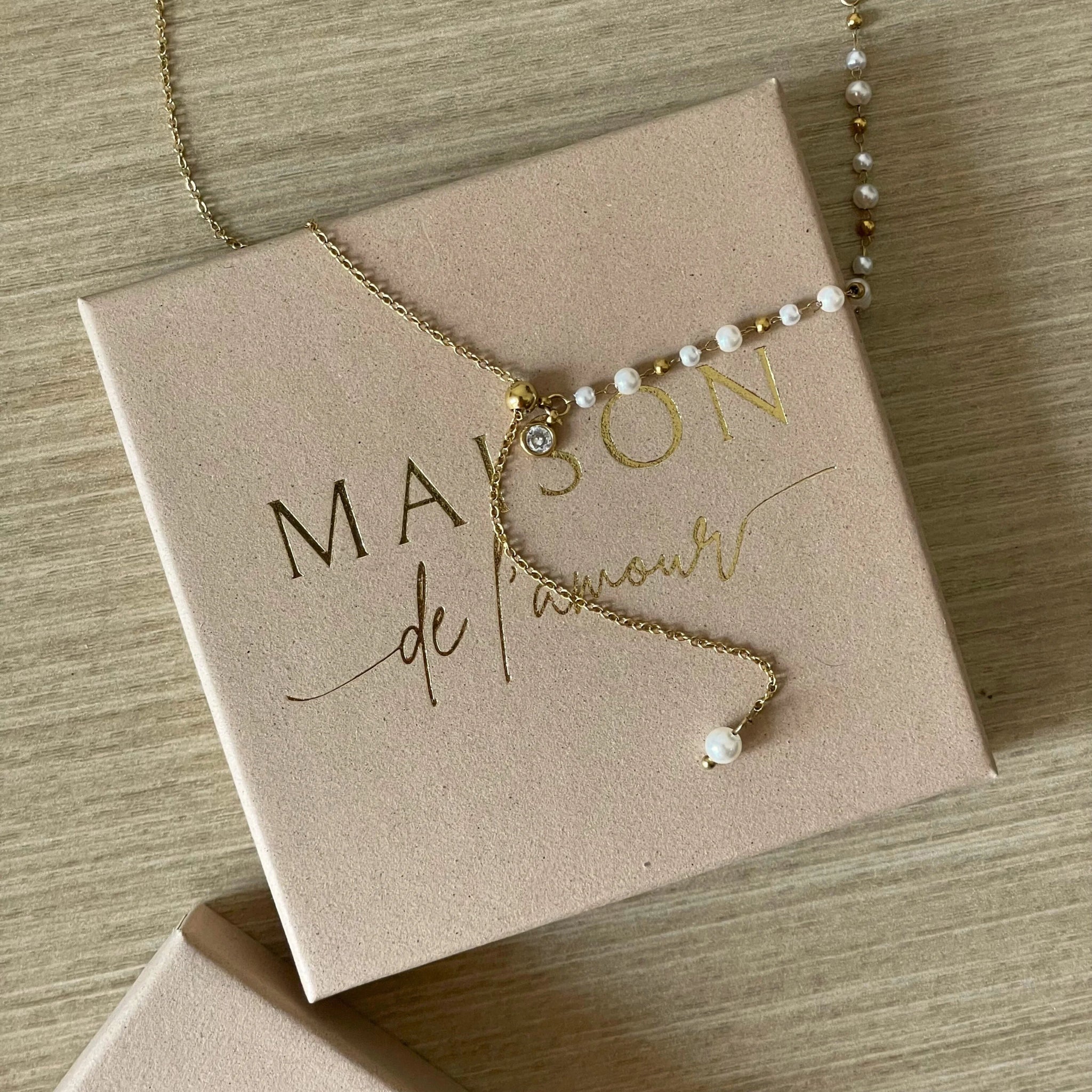 Collier fin style chapelet avec perles et chaîne pendante présenté sur sa boîte cadeau Maison de l'Amour.