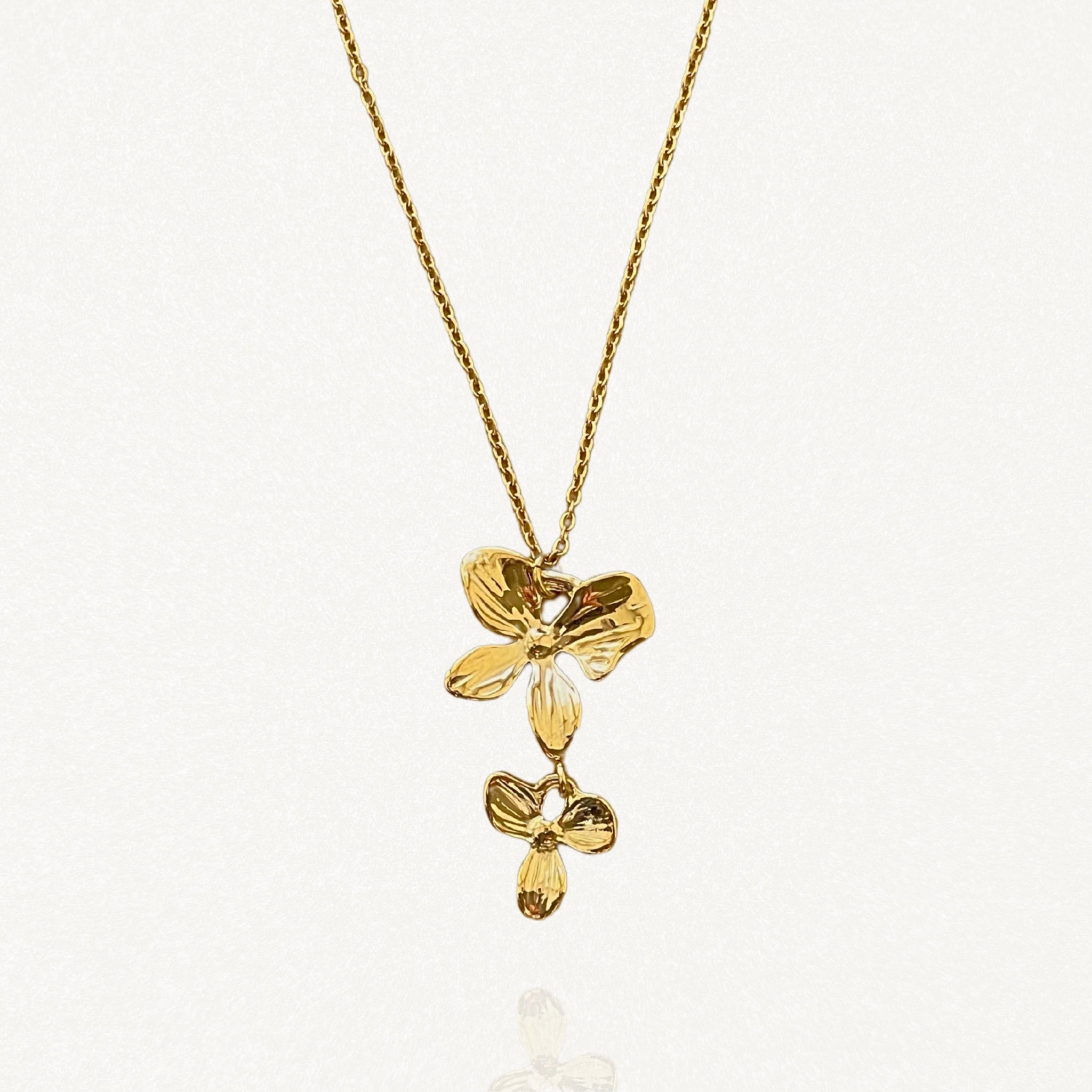 Gros plan sur le pendentif composé de deux fleurs dorées superposées sur fond blanc.