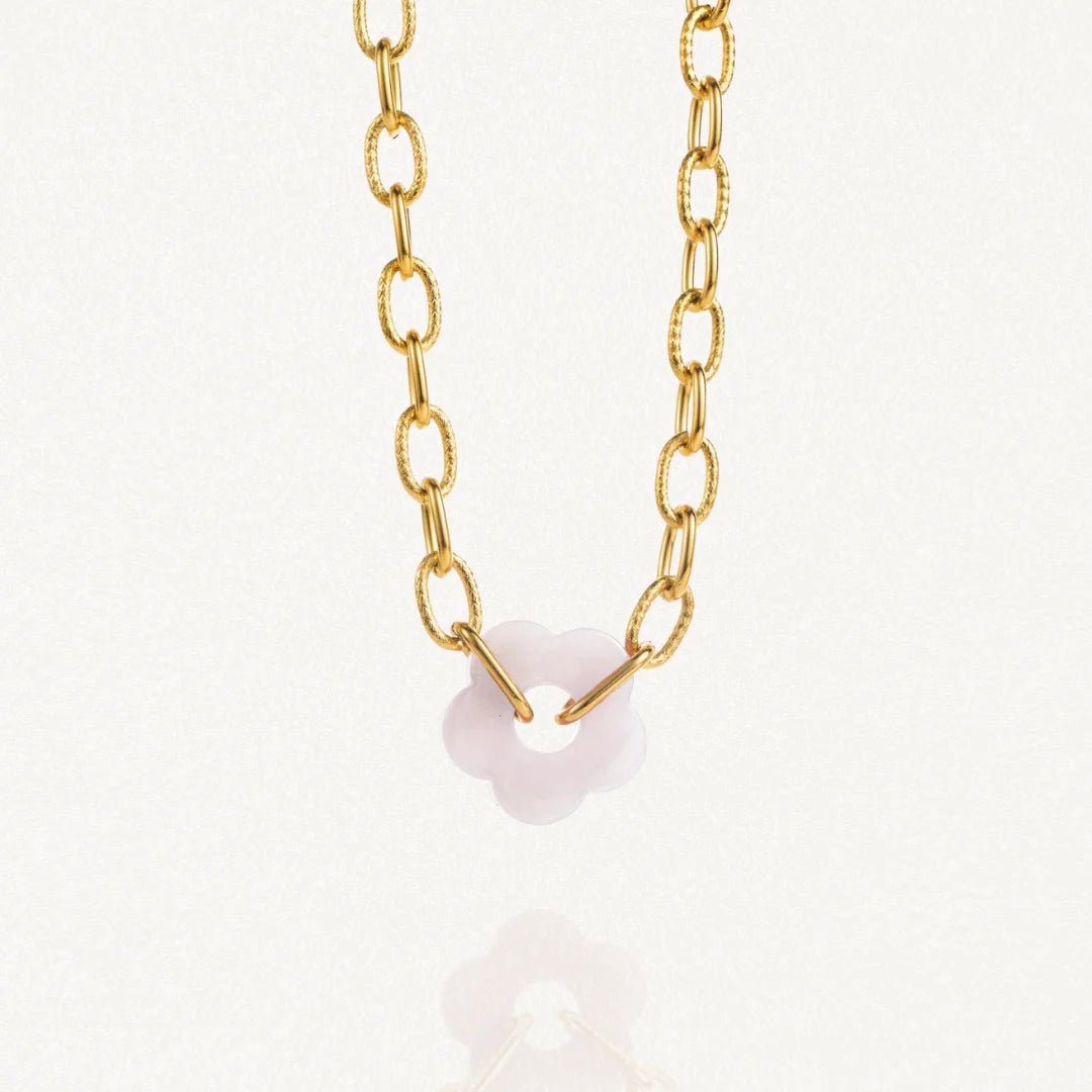 Vue d'ensemble collier grosse maille doré avec pendentif fleur blanche sur fond blanc.