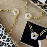 Duo de colliers à fleurs (blanc et rose) posés sur une pochette léopard et leur boîte cadeau.