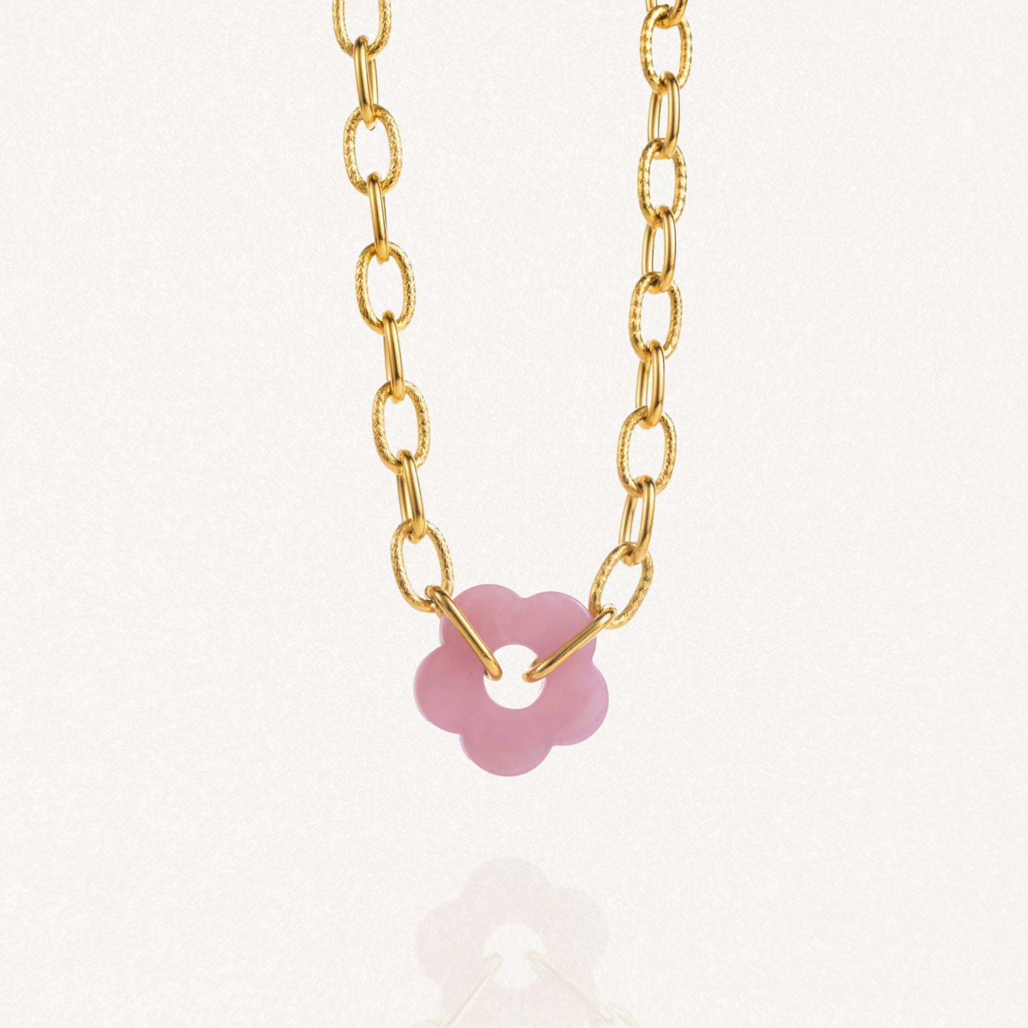 Vue d'ensemble collier grosse maille doré avec pendentif fleur rose sur fond blanc."