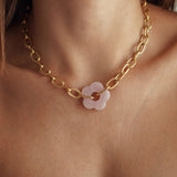 Collier grosse maille ovale en acier inoxydable doré avec pendentif central fleur rose pâle porté au cou.