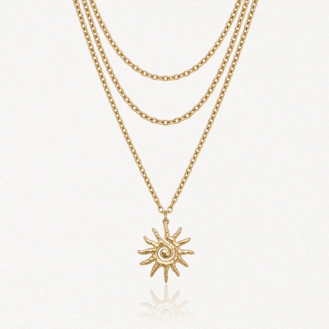 Collier trois rangs en acier inoxydable doré, pendentif soleil stylisé avec spirale et rayons.