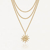 Collier trois rangs en acier inoxydable doré, pendentif soleil stylisé avec spirale et rayons.