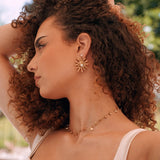 Collier fin en acier inoxydable doré avec petits pendentifs feuilles et disques, porté sur le cou d'une femme.