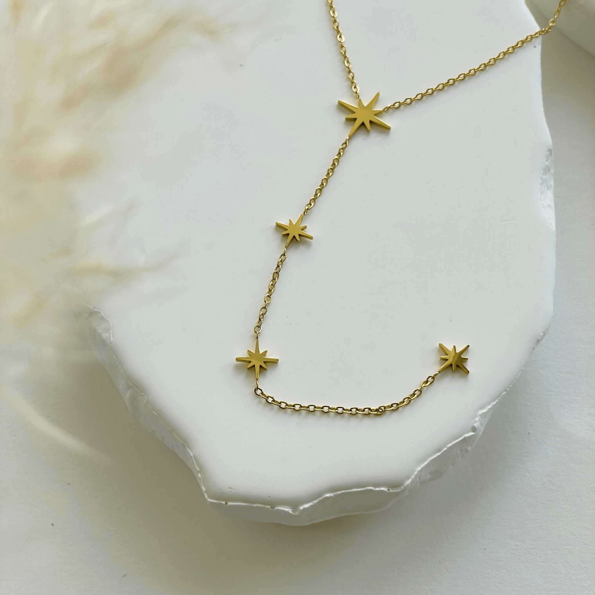 Gros plan sur la chaîne fine et les breloques étoiles du collier Louna posé sur un support.
