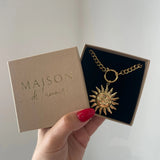 Collier pendentif soleil à visage en acier inoxydable doré présenté dans sa boîte cadeau Maison de l'Amour.