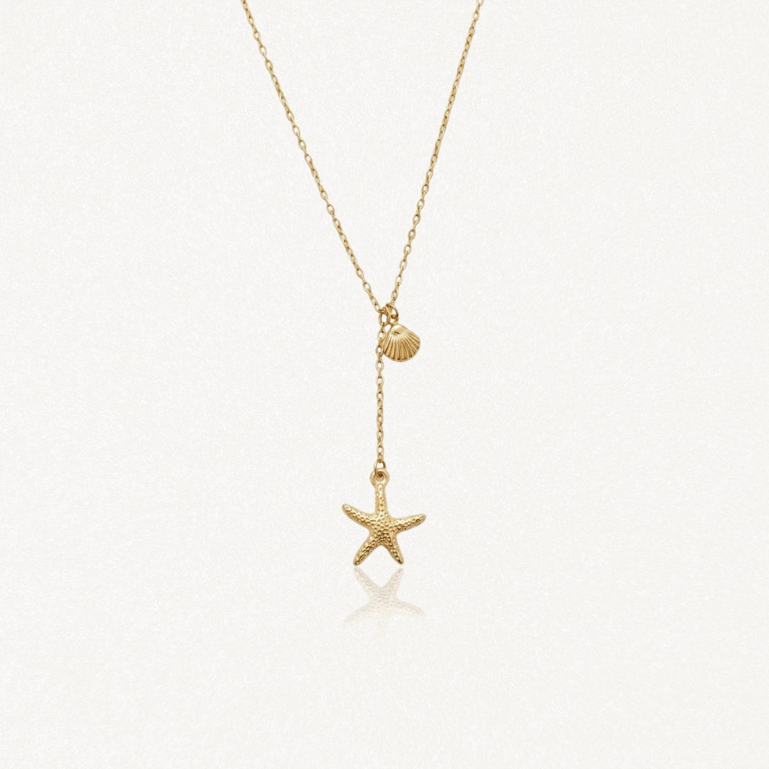 Collier lariat acier inoxydable doré avec pendentifs coquillage et étoile de mer, sur fond blanc.