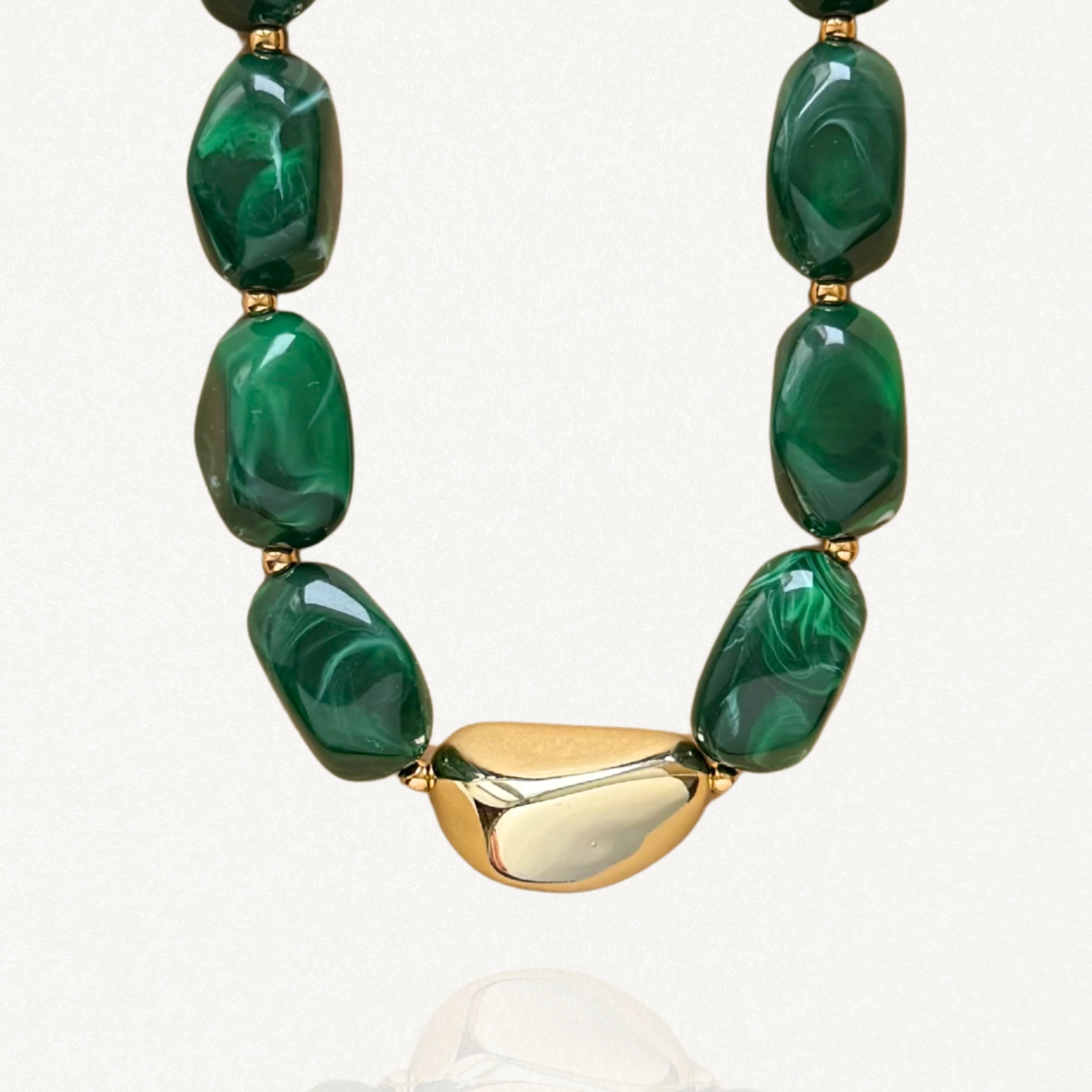Collier MAISON DE L'AMOUR avec grosses perles vertes marbrées effet malachite et pièce centrale dorée en acier inoxydable sur fond blanc.