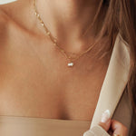 Collier double rang en acier inoxydable doré mariant une chaîne maille serpent plate et une chaîne fine avec pendentif perles blanches.