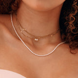 Colliers superposés: 2 en acier inoxydable doré avec perles pendantes, 1 collier de perles fines sur le cou d'une femme.