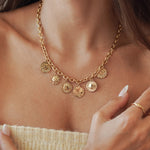 Collier chaîne grosse maille en acier inoxydable doré orné de 5 breloques médailles et soleils, porté au cou.