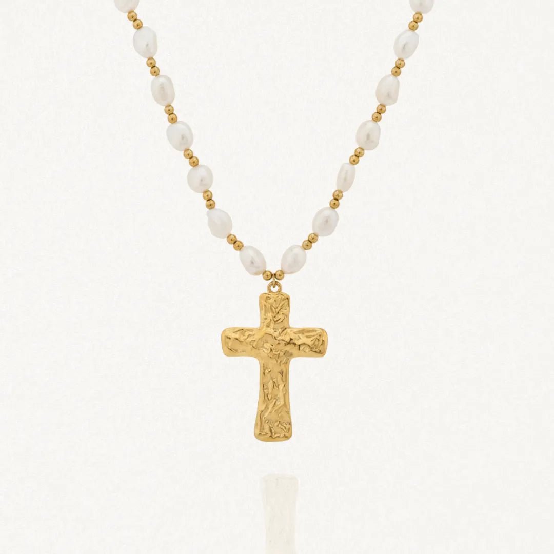 Collier avec une chaîne composée de perles blanches baroques et de petites billes dorées. Le pendentif est une croix dorée à la surface texturée et irrégulière.