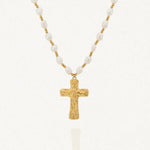 Collier avec une chaîne composée de perles blanches baroques et de petites billes dorées. Le pendentif est une croix dorée à la surface texturée et irrégulière.