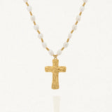 Collier avec une chaîne composée de perles blanches baroques et de petites billes dorées. Le pendentif est une croix dorée à la surface texturée et irrégulière.
