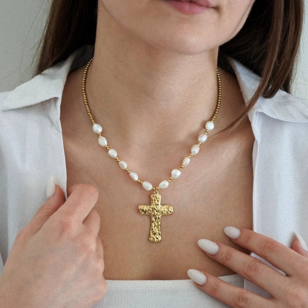 Collier doré avec perles blanches baroques et pendentif croix martelée sur une femme en chemise blanche.