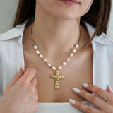 Collier doré avec perles blanches baroques et pendentif croix martelée sur une femme en chemise blanche.