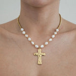 Collier à perles baroques blanches et perles dorées, pendentif croix martelée doré, porté sur un cou.