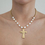 Collier à perles baroques blanches et perles dorées, pendentif croix martelée doré, porté sur un cou.
