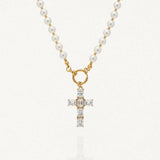 Collier doré en acier inoxydable avec une chaîne composée de perles rondes blanches, reliée par un fermoir toggle. Un pendentif en forme de croix est suspendu, entièrement pavé de zircons rectangulaires brillants.