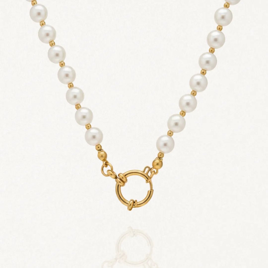 Collier de perles blanches rondes et billes dorées avec fermoir anneau-ressort doré sur fond clair.