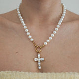 Collier perles blanches, petites billes dorées, pendentif croix or serti de zircons rectangulaires, porté par une femme.