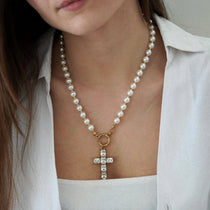Collier de perles blanches et billes dorées avec pendentif croix en métal doré serti de pierres claires rectangulaires.