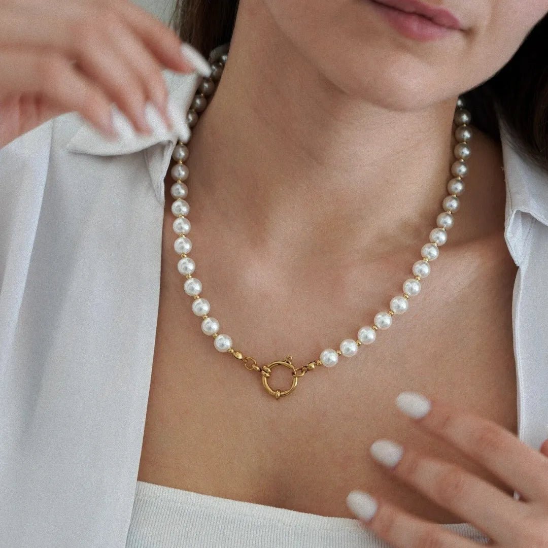 Collier de perles blanches, séparées par de petites perles dorées, avec un grand fermoir anneau doré au centre, porté par une femme.