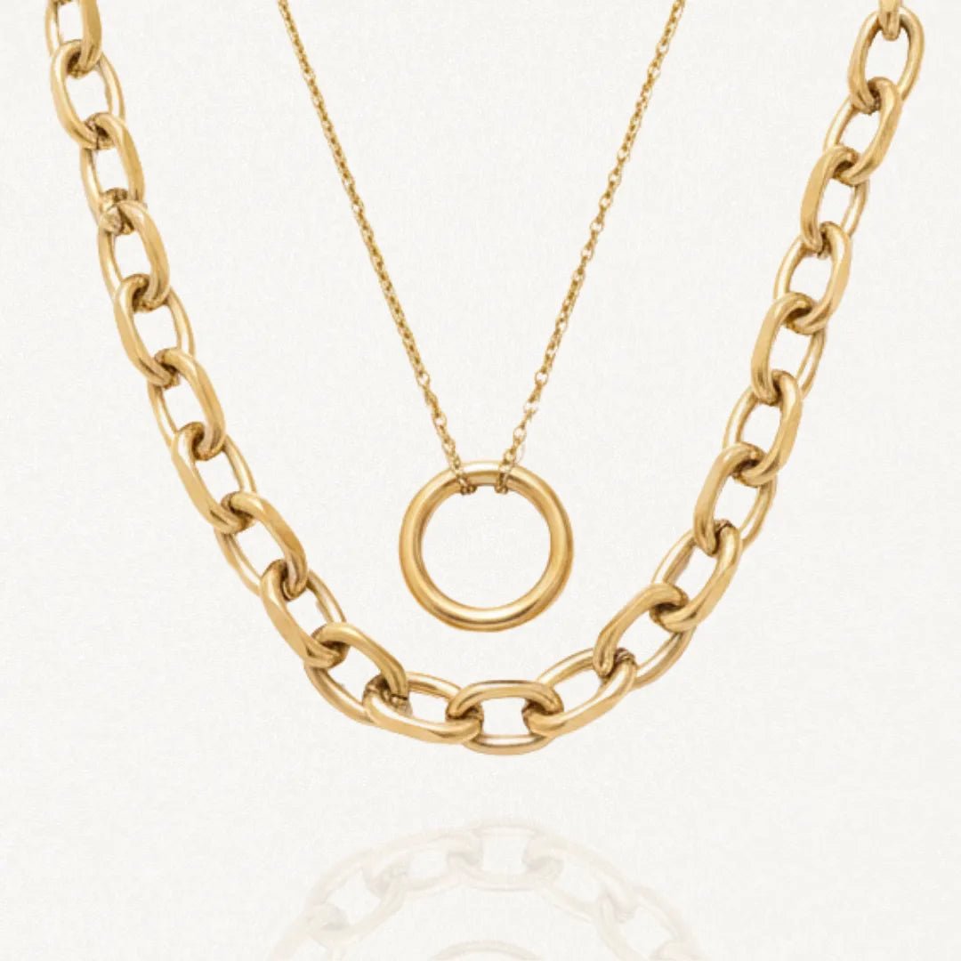 Double collier doré en acier inoxydable. Il se compose d'une chaîne épaisse à maillons ovales et d'une chaîne fine avec un pendentif anneau lisse.