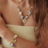 Collier ex-voto en acier inoxydable doré porté en parure avec son bracelet assorti à breloques.